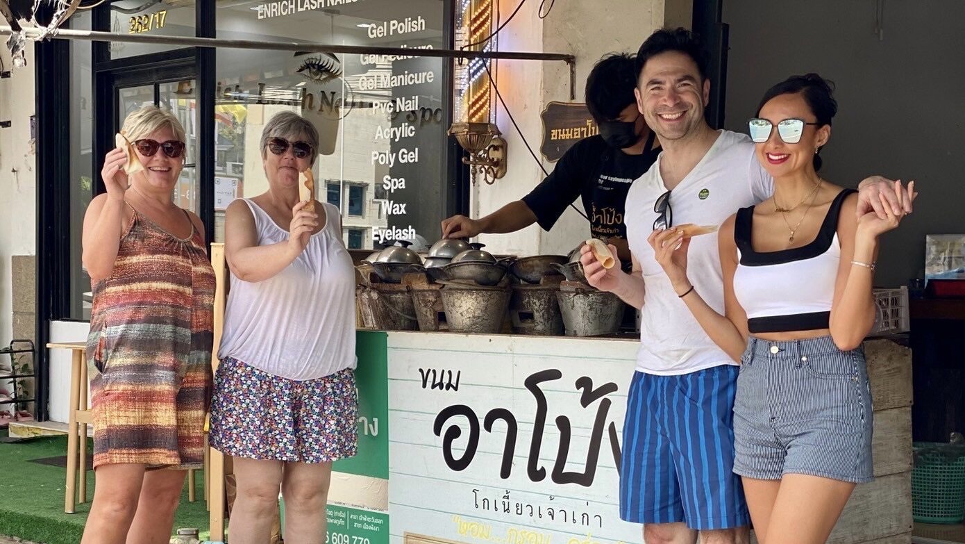 Travelers trying fresh A-Pong coconut crepes and Pao Lang grilled sticky rice